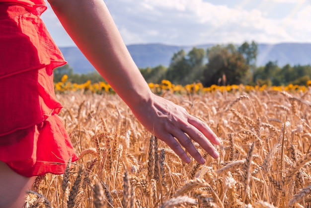 Primer plano de una mujer con un vestido rojo en un campo de trigo en un día soleado