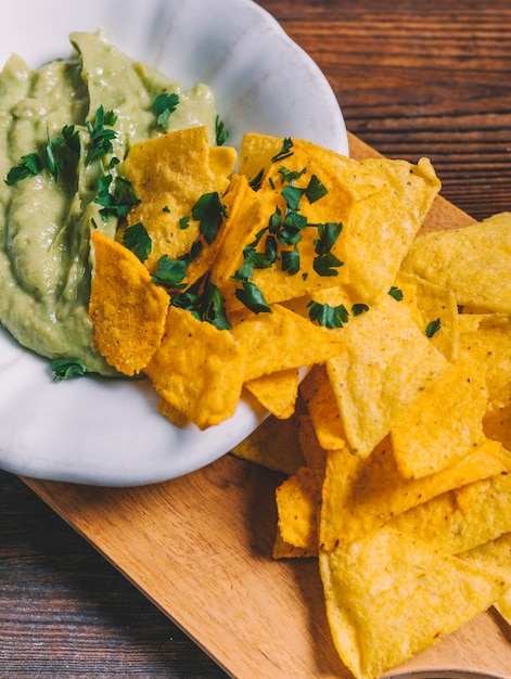 Primer plano de nachos mexicanos y guacamole en un tazón en tabla de cortar de madera