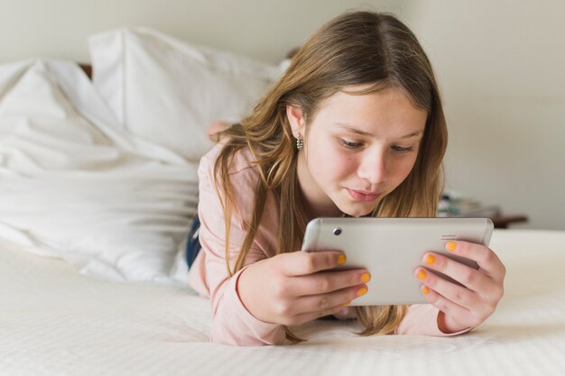 Primer plano de una niña acostada en la cama mirando el teléfono móvil