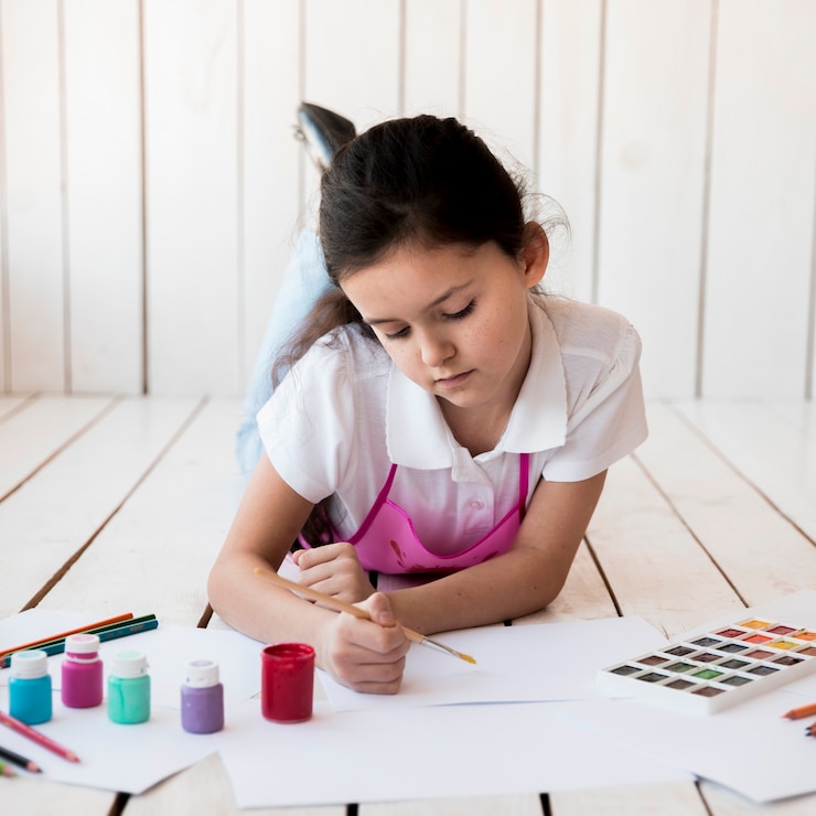 Foto gratuito primer plano de una niña acostada sobre tablones de madera pintando sobre el papel blanco la brocha