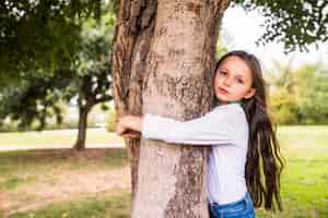 Foto gratuita primer plano de una niña adorable abrazando el tronco del árbol