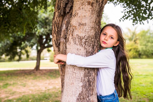 Primer plano de una niña adorable abrazando el tronco del árbol