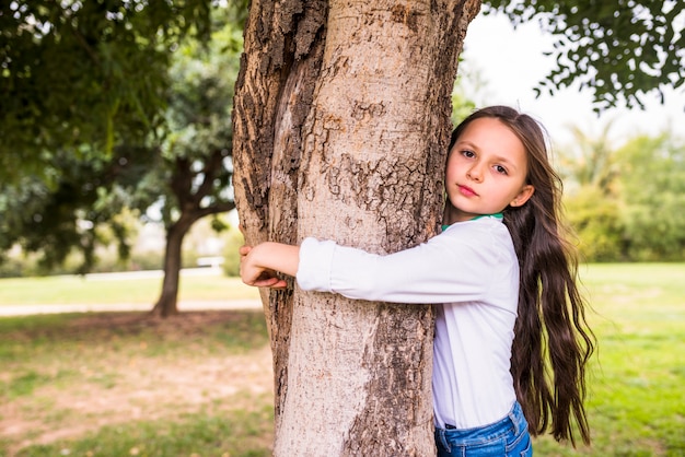 Primer plano de una niña adorable abrazando el tronco del árbol