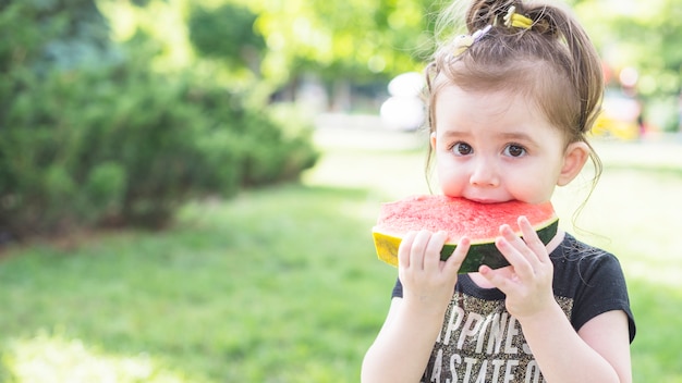 Primer plano de una niña comiendo sandía en el parque