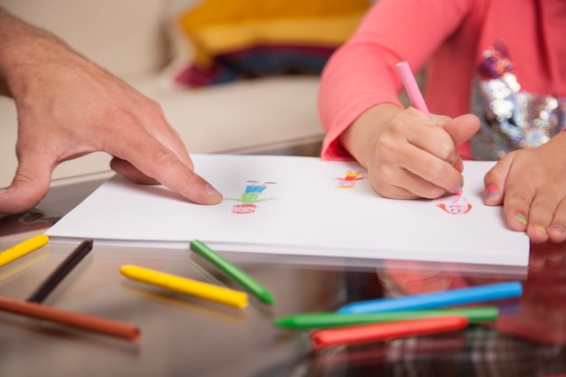 Primer plano de niña dibujando y de su padre señalando