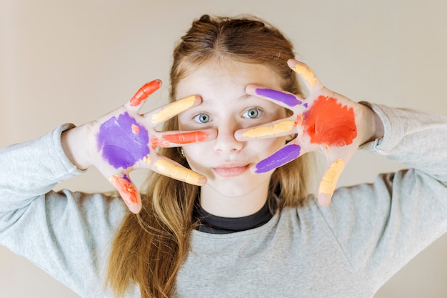 Foto gratuita primer plano de una niña con las manos pintadas mirando la cámara