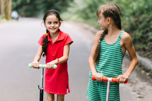 Primer plano de una niña mirando a su amiga mientras monta scooters en la carretera