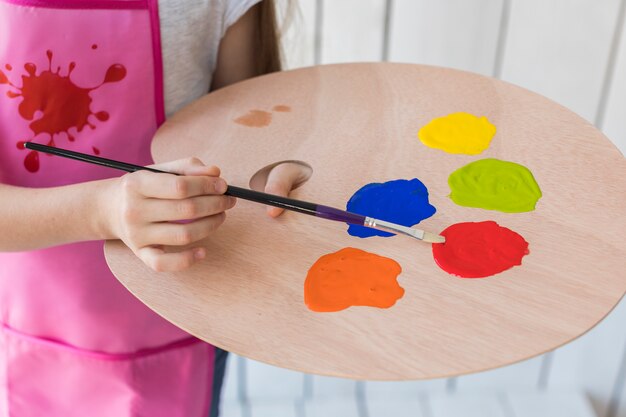 Primer plano de una niña que mezcla la pintura con pincel en la paleta de madera