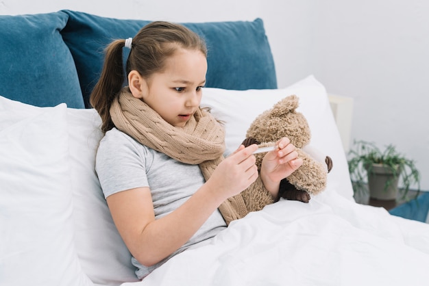 Primer plano de una niña que sufre de frío y fiebre mirando la temperatura en el termómetro