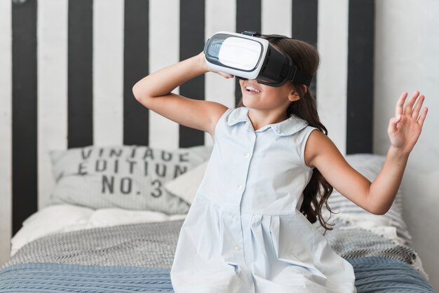 Primer plano de una niña sentada en la cama con gafas de realidad virtual