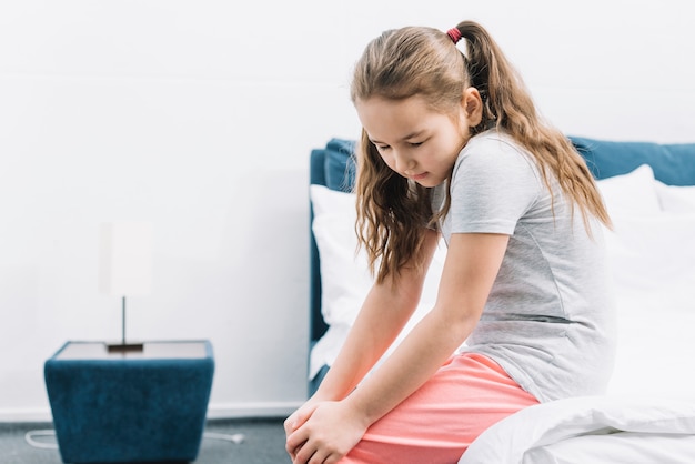 Foto gratuita primer plano de una niña sentada en la cama sufriendo de dolor de rodilla