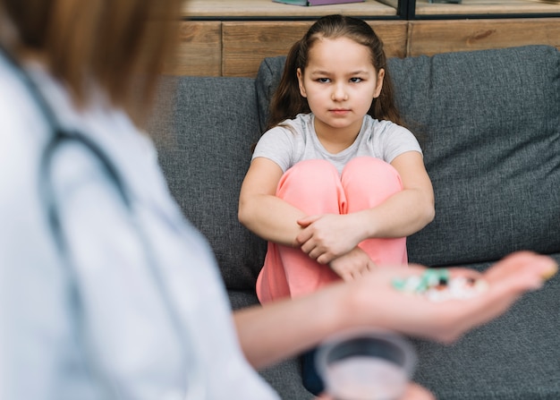 Primer plano de niña seria sentado en el sofá mirando médico dando medicina