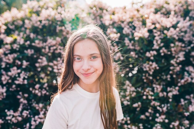 Primer plano de una niña sonriente bonita de pie contra las plantas de flor