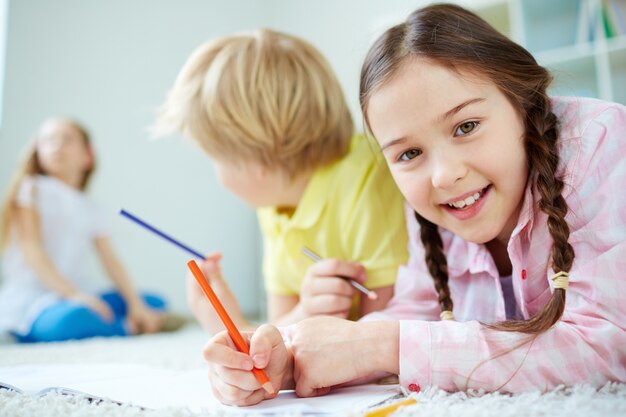 Primer plano de niña sonriente con un lápiz naranja