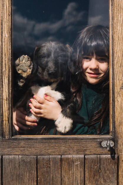 Primer plano de una niña con su perro mirando a través de la puerta de cristal transparente