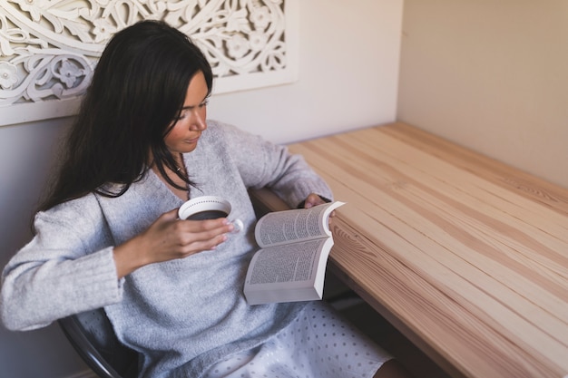 Foto gratuita primer plano de una niña con taza de café sentado en el libro de lectura de la silla