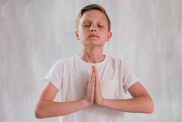 Primer plano de un niño cerrando los ojos haciendo meditación contra un muro de hormigón