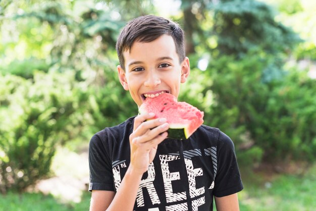 Primer plano de un niño comiendo rebanada de sandía en el parque