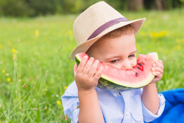 Primer plano de un niño comiendo rebanada de sandía en el parque