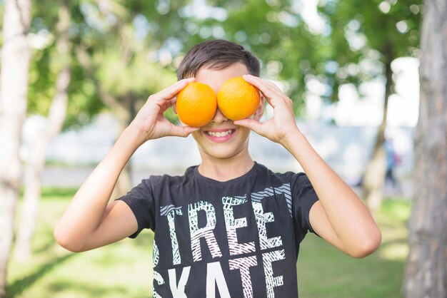 Primer plano de niño cubriéndose los ojos con naranjas