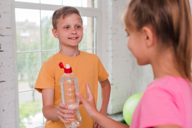 Primer plano de un niño dando botella de agua a su amigo