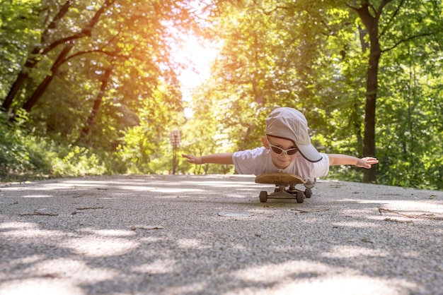 Primer plano de un niño con gafas de sol y una gorra tumbado en una patineta en un parque