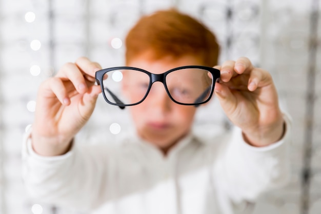 Primer plano del niño mostrando anteojos de montura negra en la tienda de óptica