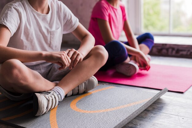 Primer plano de un niño y una niña sentados en una colchoneta de ejercicios gris y rosa