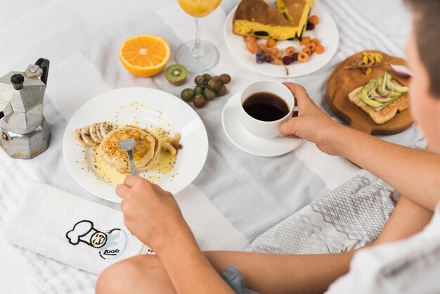 Primer plano de un niño con panqueques y café en la cama