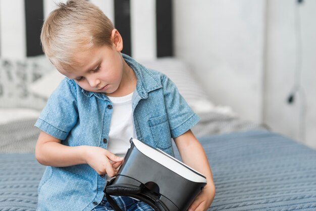 Primer plano de un niño pequeño sentado en la cama ajustando gafas de realidad virtual