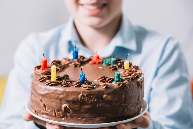 Primer plano de un niño sonriente mostrando pastel de chocolate decorado con velas de colores