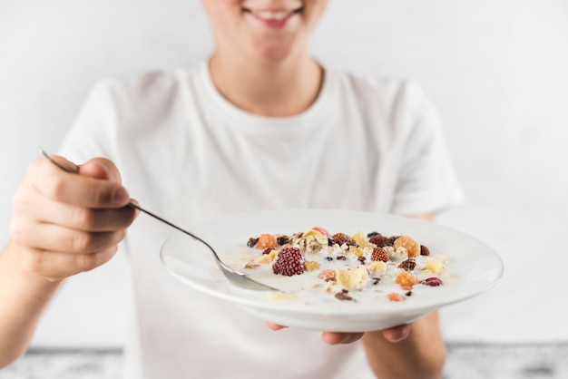 Primer plano de un niño sonriente con placa de gachas de avena y cuchara en las manos