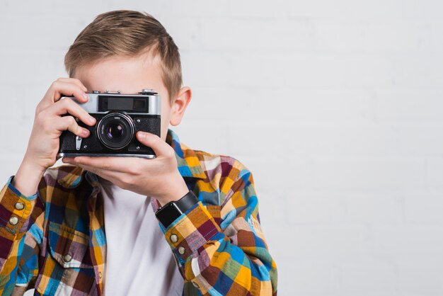 Primer plano de niño tomando foto con cámara vintage contra fondo blanco