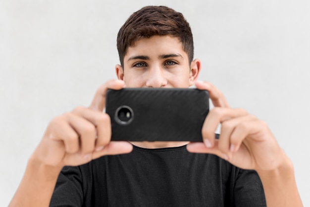 Primer plano de niño tomando fotos a través del teléfono celular contra el fondo blanco