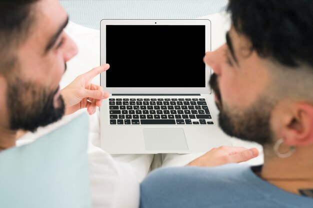 Primer plano de novio mirando al hombre que señala el dedo sobre el monitor de la computadora portátil