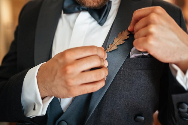 Primer plano del novio vistiéndose el día de su boda y poniendo un broche de decoración en la solapa de su chaqueta