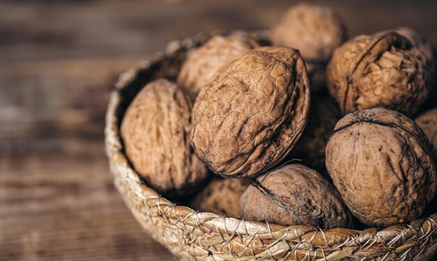 Primer plano de nueces enteras en un recipiente de mimbre sobre un fondo de madera