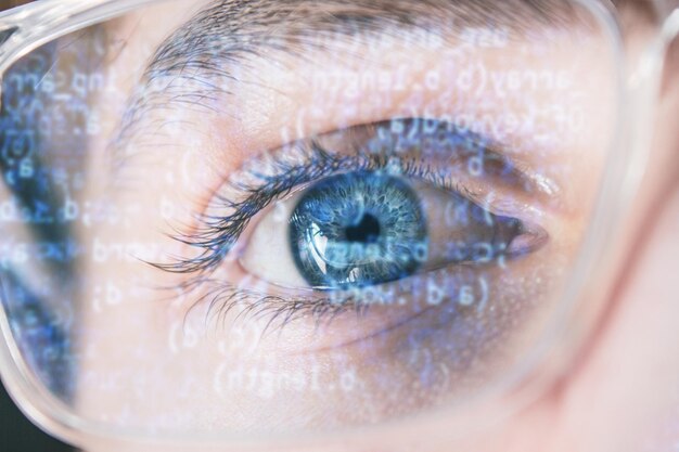 Primer plano del ojo azul del hacker con gafas ópticas con código de datos reflejado en el cristal