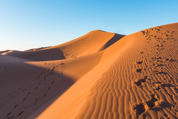 Primer plano de ondas de arena y pistas sobre dunas de arena en un desierto contra el cielo azul claro