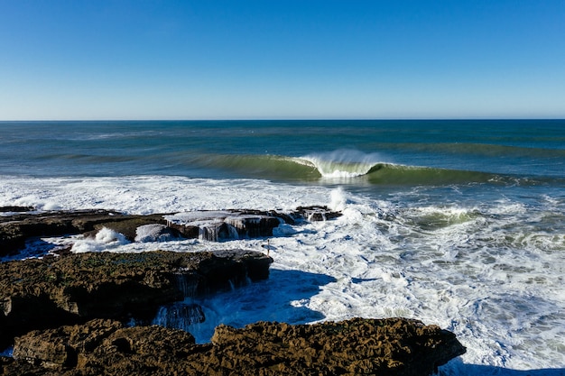 Foto gratuita primer plano de ondas de espuma golpeando la costa rocosa en un día soleado