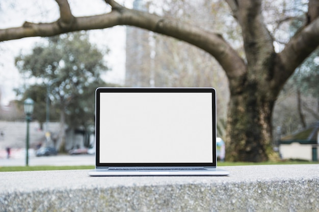 Primer plano de un ordenador portátil con pantalla en blanco en blanco en el banco en el parque