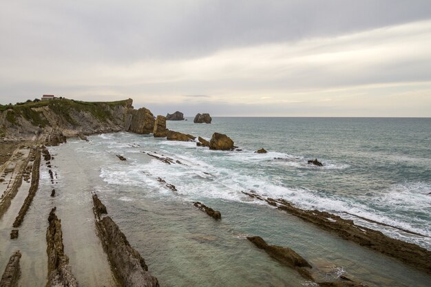 Primer plano de una orilla del acantilado cerca de un mar ondulado bajo un cielo nublado