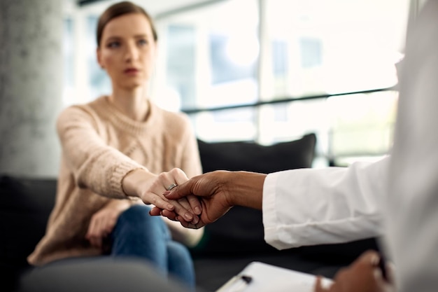 Primer plano de una paciente y un profesional de la salud mental tomándose de la mano durante la psicoterapia