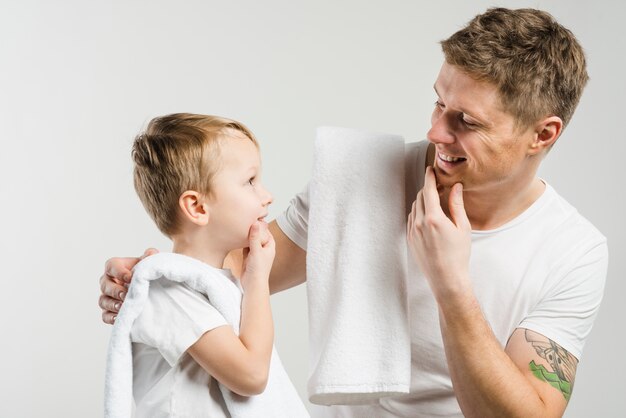 Primer plano de padre e hijo tocando su barbilla con las manos mirando el uno al otro contra el fondo blanco