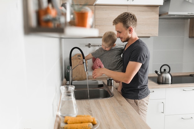Primer plano de un padre con su hijo de pie cerca del fregadero de la cocina