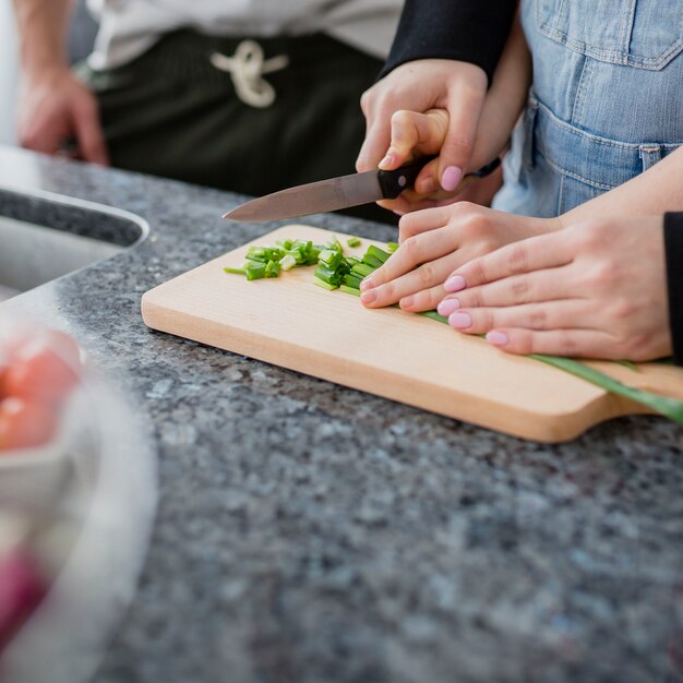 Primer plano de los padres que ayudan a la niña a cortar verduras