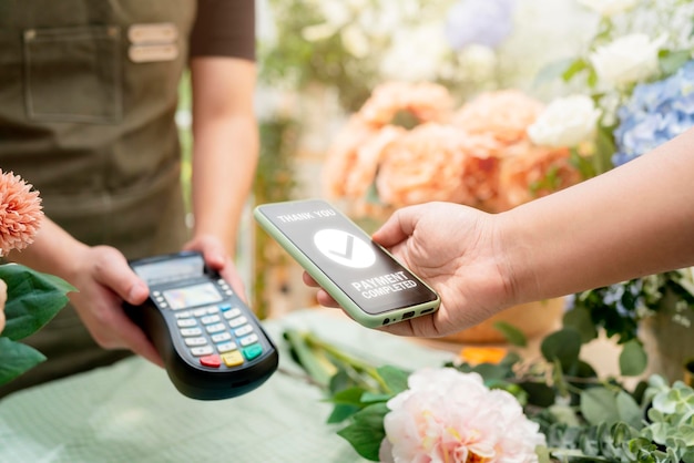 Primer plano de pago fácil con tarjeta de crédito o aplicación de teléfono inteligente Trabajadores de invernadero que venden flores en maceta Pago sin contacto con el cliente de la tarjeta de crédito en el mostrador mediante el pago sin contacto con código QR