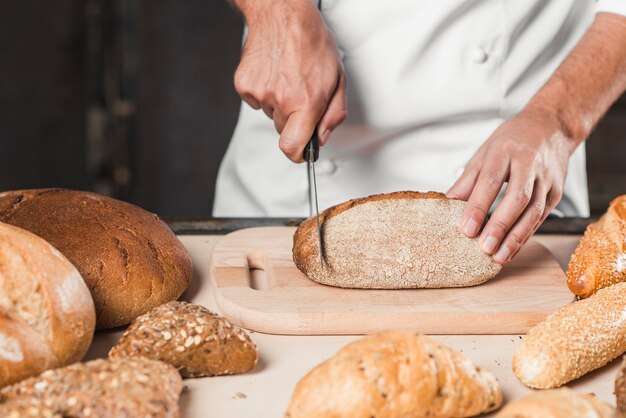 Primer plano de pan de corte de panadero masculino con cuchillo en la tajadera