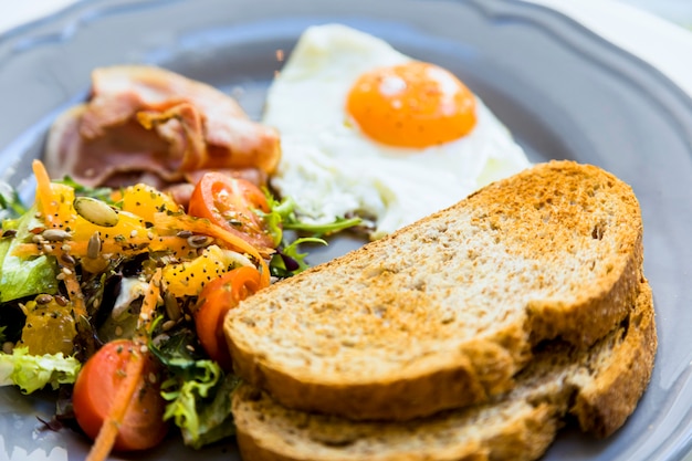 Primer plano de pan tostado; huevos fritos; Ensalada y tocino servido en plato cerámico.