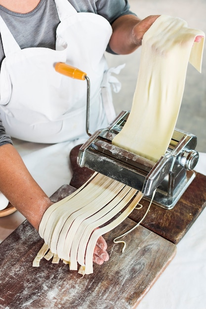 Foto gratuita primer plano de panadero cortando masa cruda en tallarines en máquina de pasta